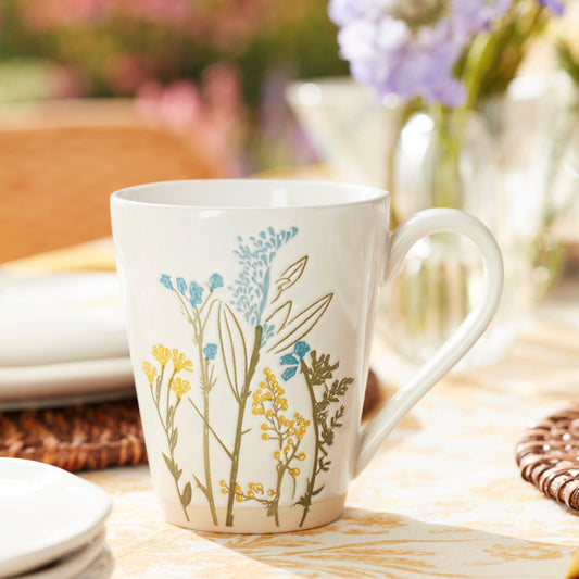 White ceramic mug with yellow and blue wildflower design on a sunlit table.